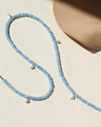 A 14k gold fill fully beaded necklace featuring blue opal gemstones and 6 small freshwater pearls. The necklace is displayed on a cream back drop. 