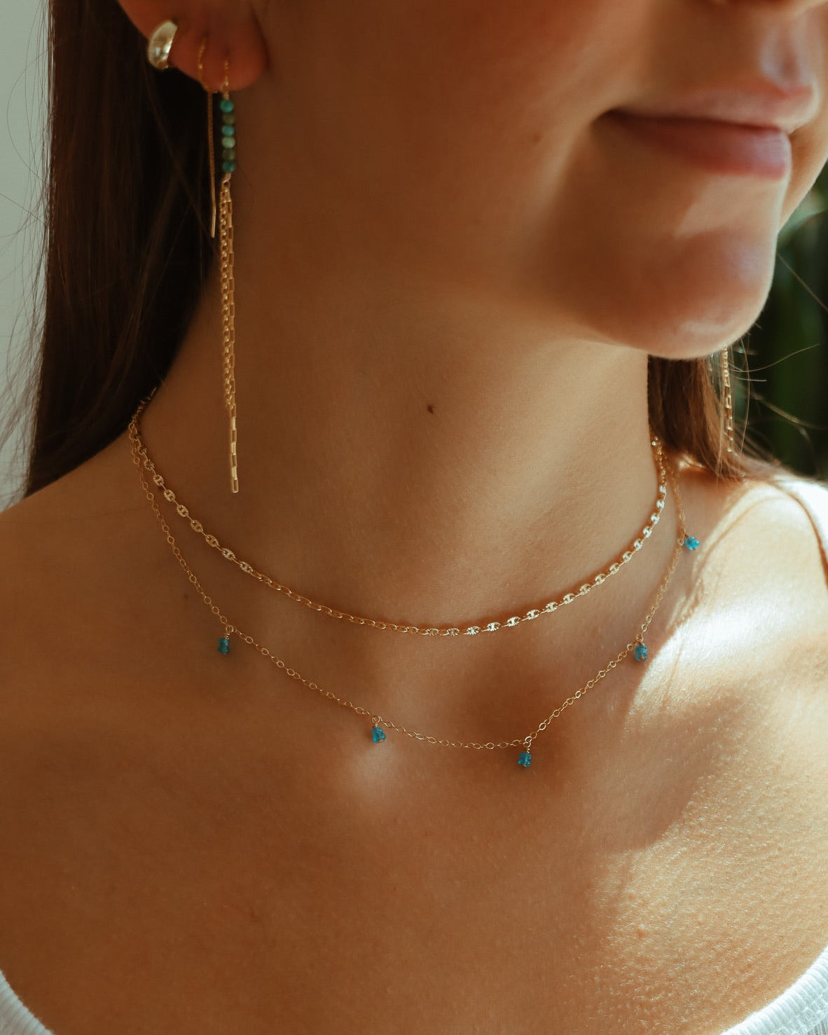 Model wearing the bluebell necklace featuring blue apatite gemstones dangling from a simple chain layered with other 14k gold filled jewelry