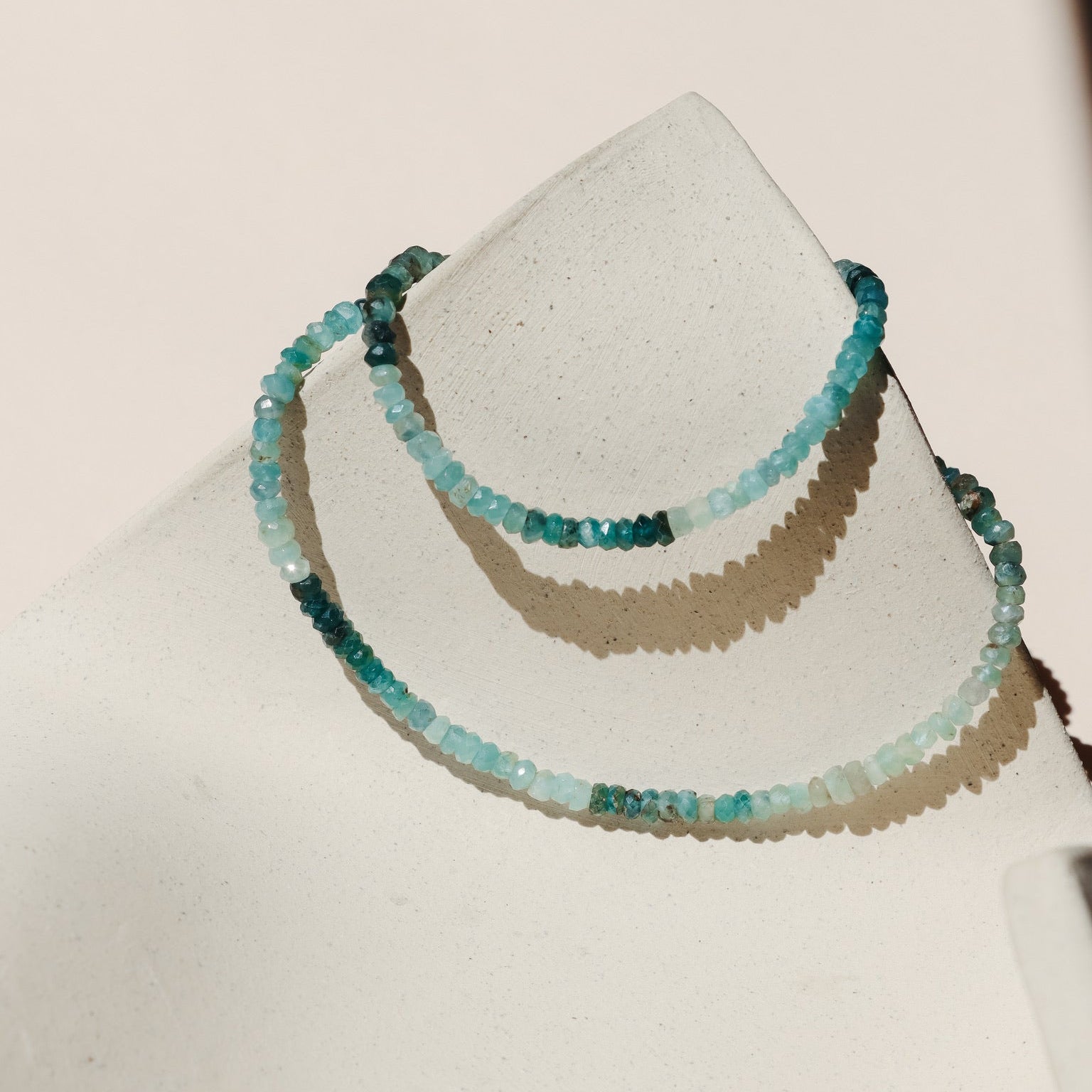 Blue Beaded necklace with faceted stones that vary from light blue to deep blue, draped on a beige dish. 