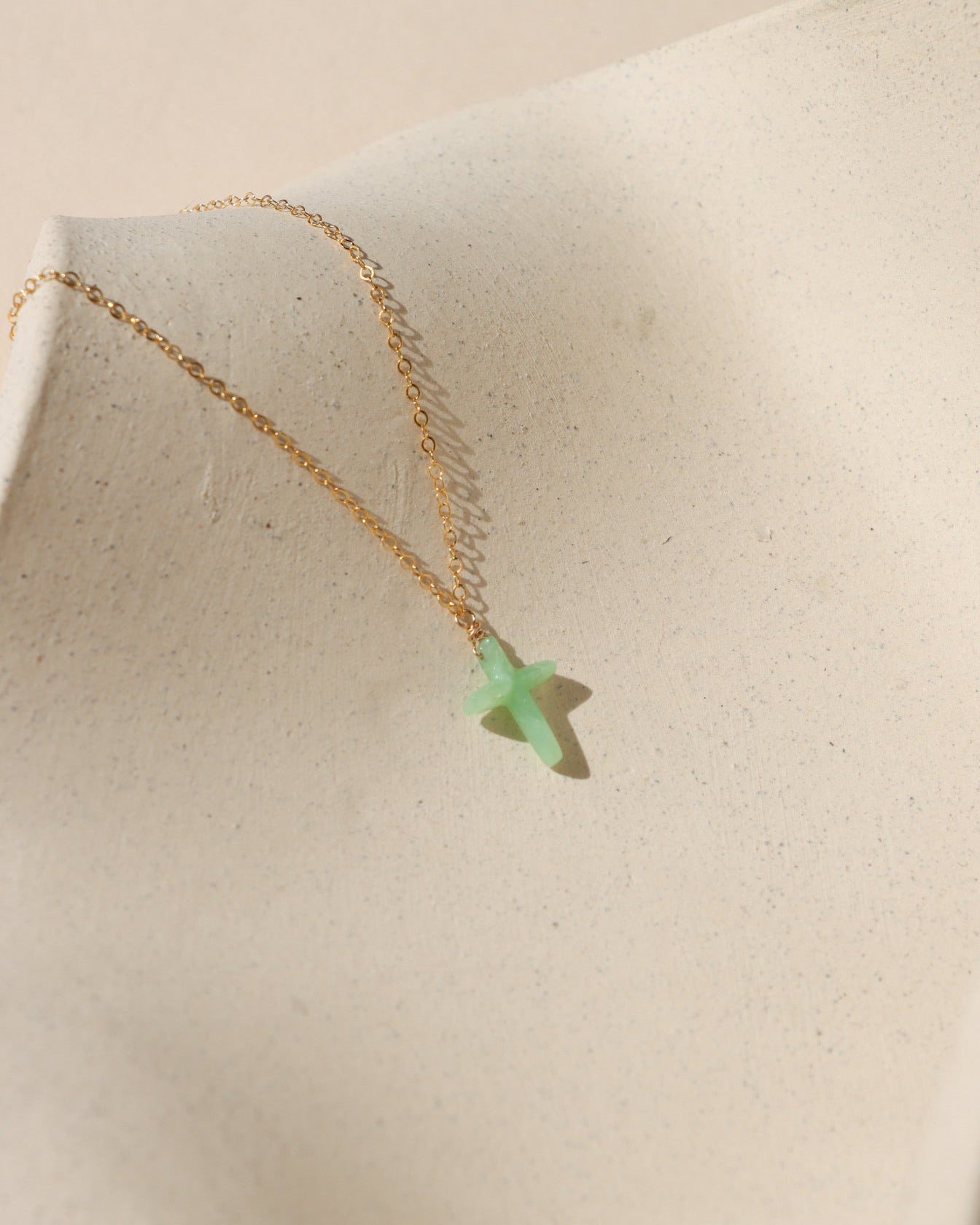 14k gold fill delicate chain necklace with Chrysophrase cross charm on a light dish