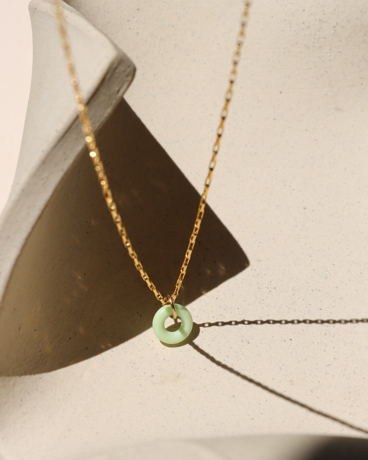 Chrysoprase donut shaped gemstone pendant attached to a 14k gold Fill chain in the sunlight