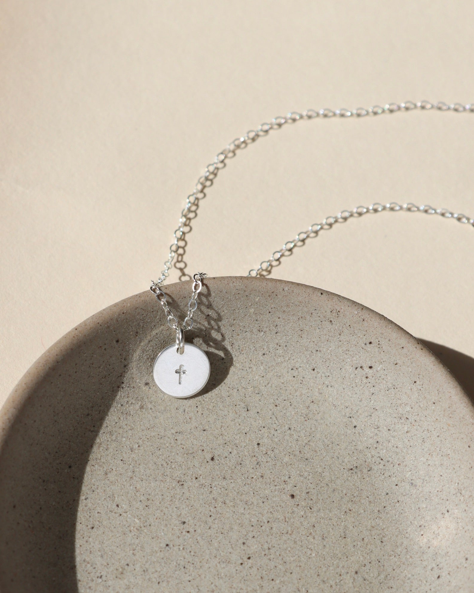 Sterling silver delicate chain necklace with a sterling silver hand stamped cross charm in the sunlight