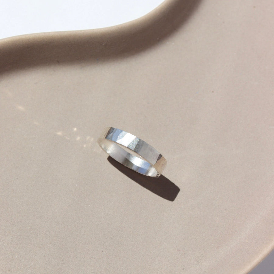 925 sterling silver cigar style ring laid on a white plate in the sunlight. This ring features a hammered band