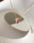 Champagne quartz necklace is laid on top of a white pot. This necklace and pot are placed in the sunlight. This necklace features the Pink Champagne Quartz gemstone connected by the simple chain. This necklace is hand made in Eau Claire Wisconsin.