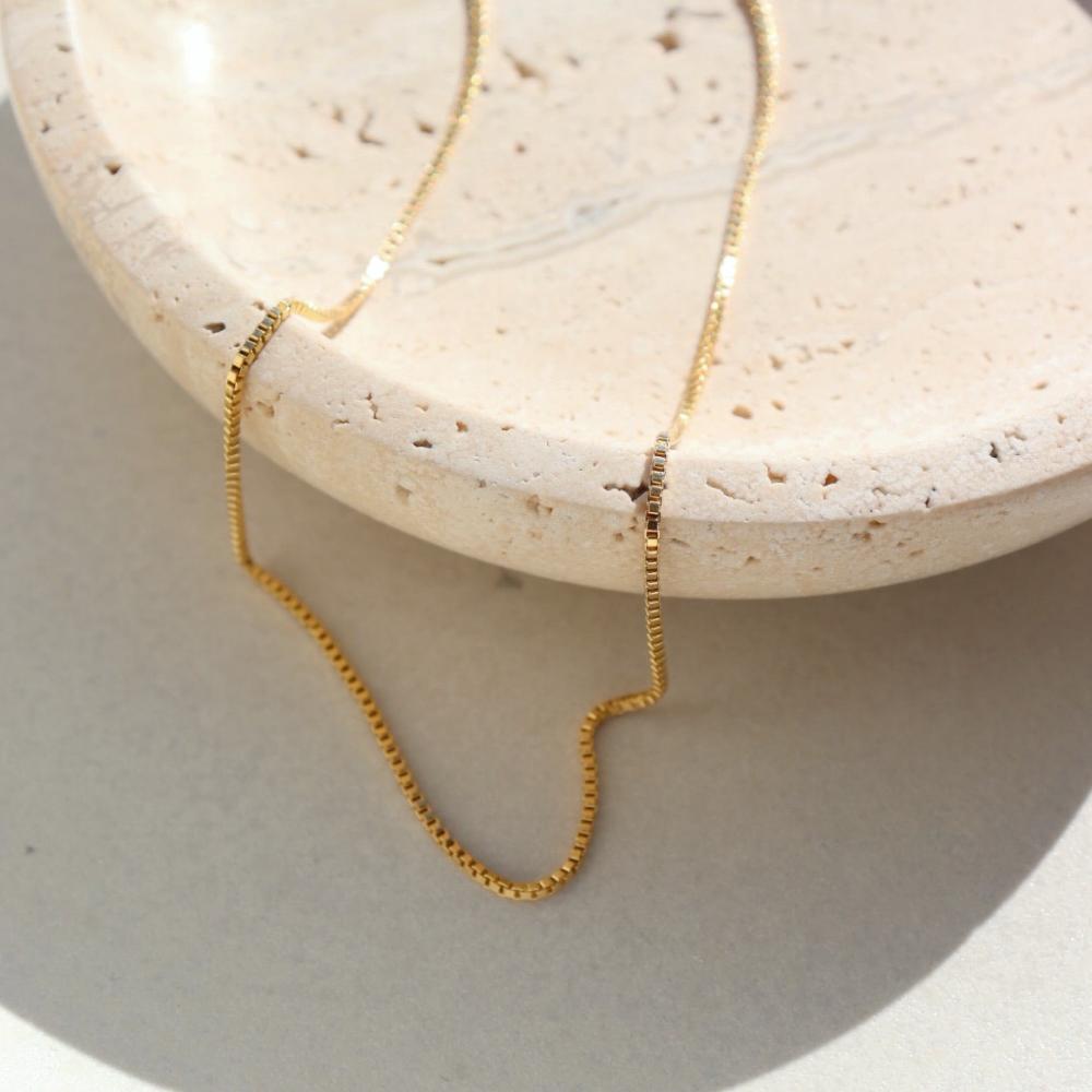 14k gold fill Necklace laid on a cream plate in the sunlight.