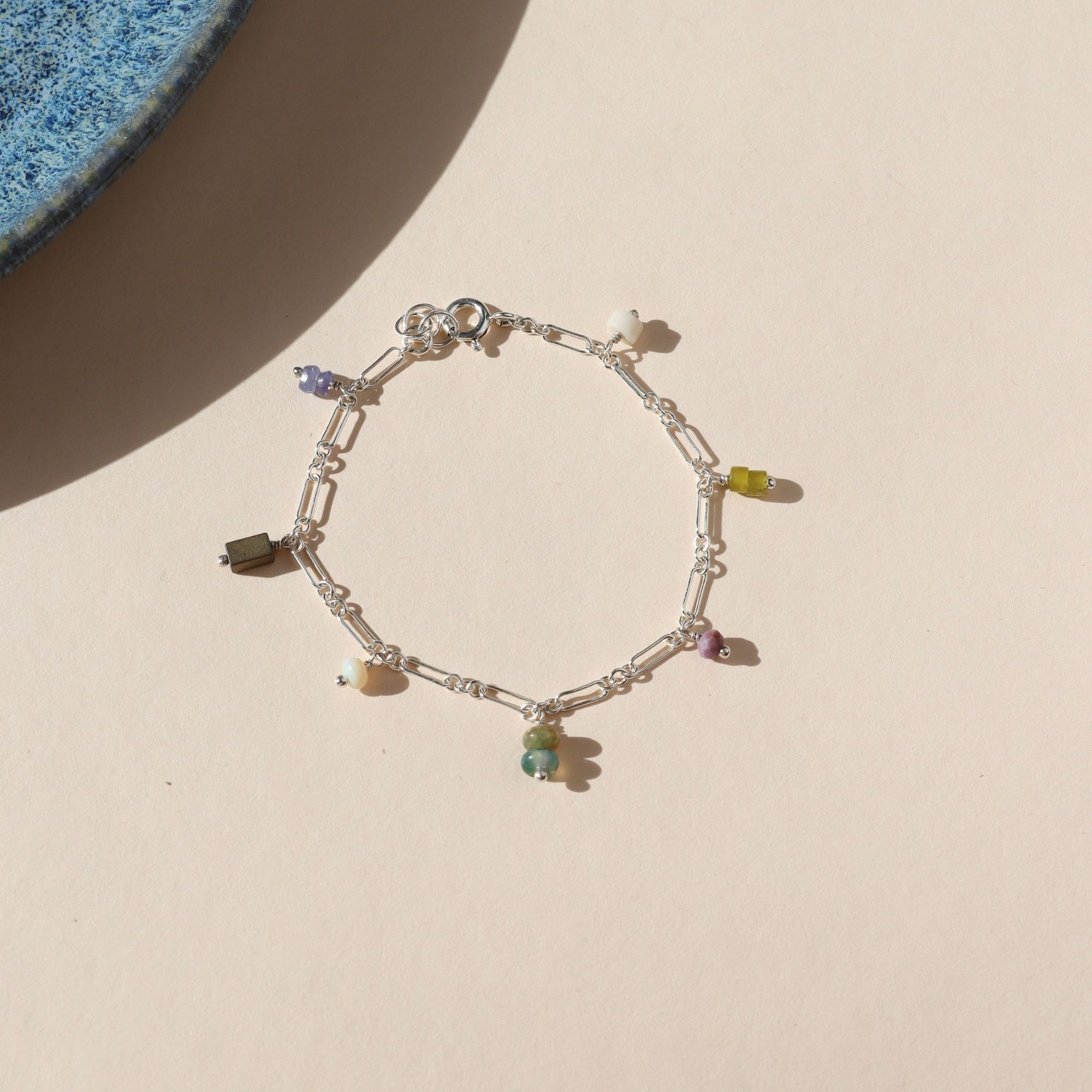 sterling silver chain bracelet with various gemstone charms on a light dish
