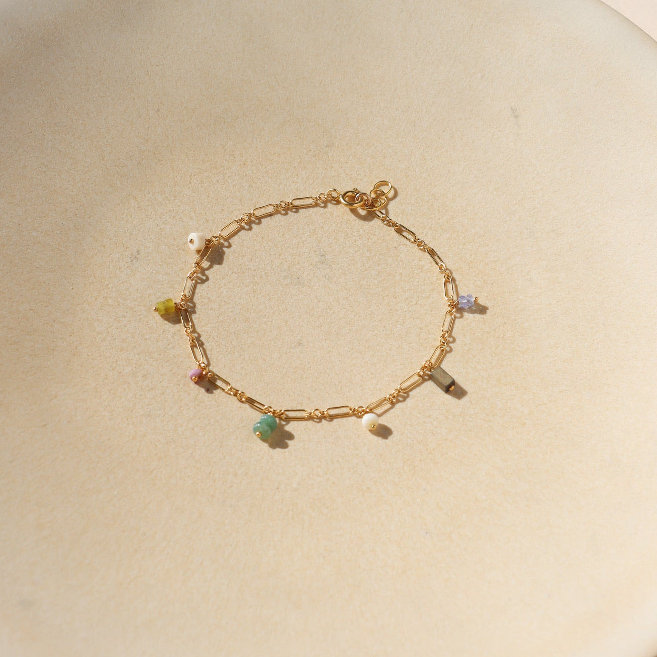 14k gold fill gemstone charm anklet with a link chain laying on a beige dish in natural light