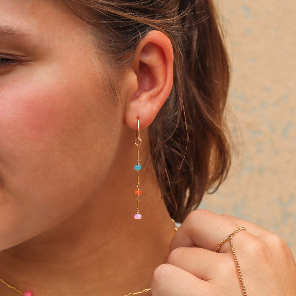 Model wearing Disco Opal Earrings featuring six multicolored opals on a bar, dot, and dash chain design in gold fill.