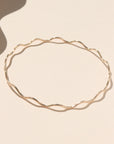 14k gold fill bangle with wave-like textured wire, displayed on a cream backdrop in natural sunlight. 