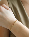 Model wearing a half and half 14k gold fill bracelet featuring a thick curb chain and a double vine chain. Also known as our Demi Alexandra and Makara chains. Model is wearing a olive green tank top. 