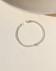 A half and half sterling silver bracelet featuring a thick curb chain and a double vine chain. Also known as our Carter and Makara chains. The bracelet is displayed on a cream back drop in the sun light. 