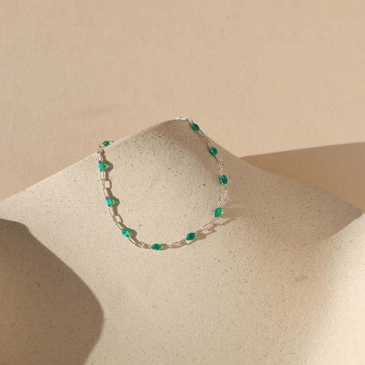 sterling silver chain bracelet with transparent emerald gemstones on a light dish 