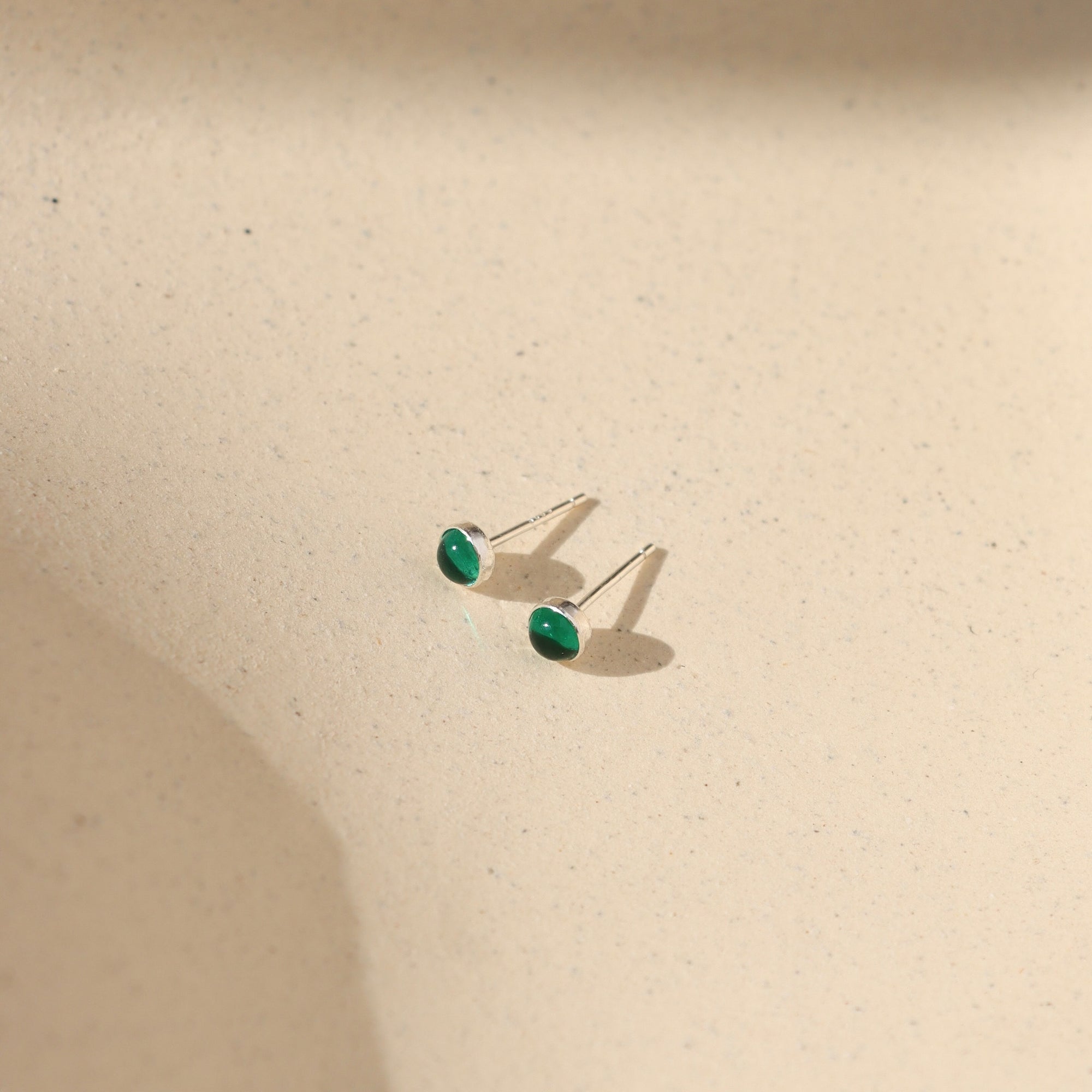 sterling silver bezel studs with 4mm emerald stones on a light background