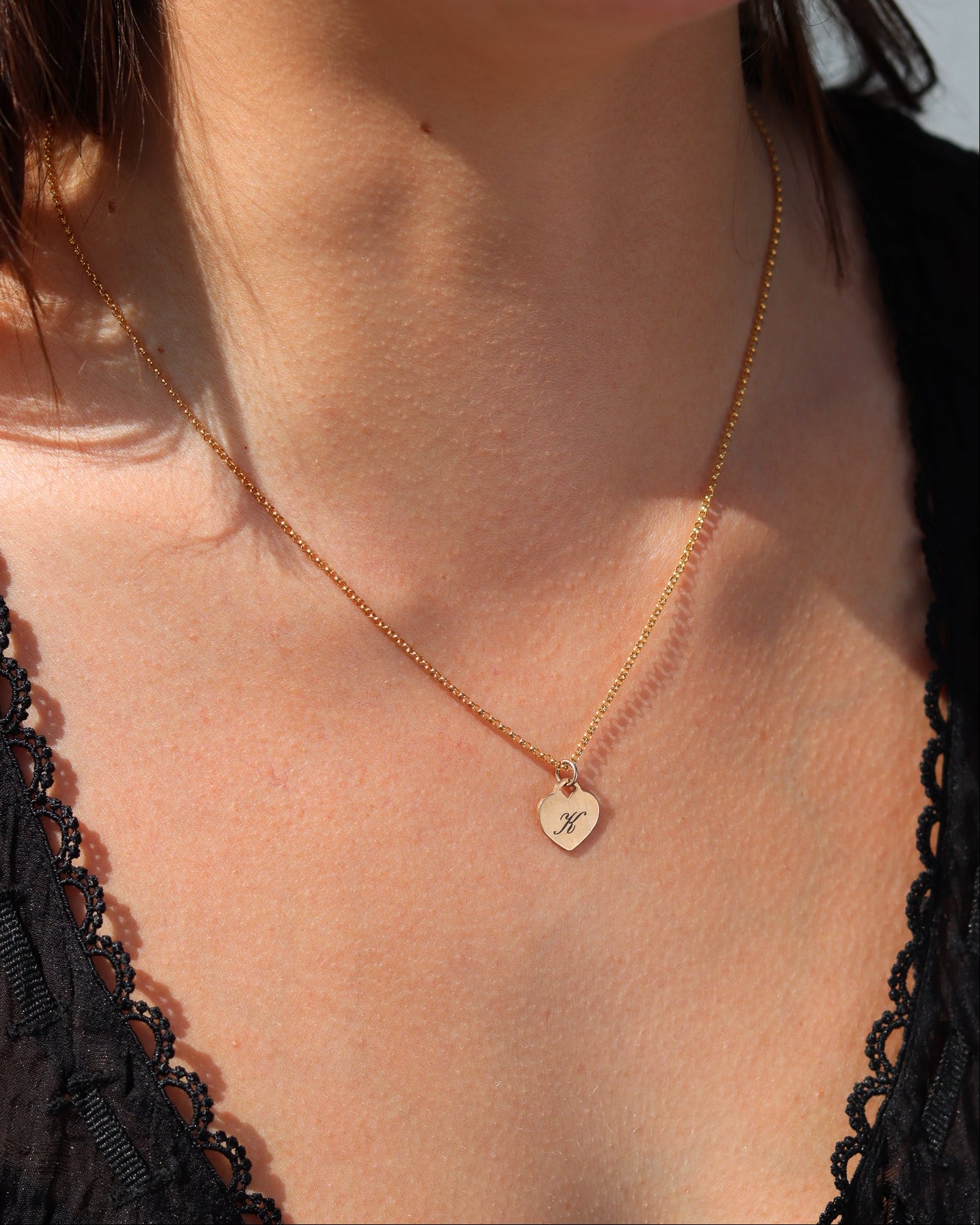 Gold heart pendant necklace engraved with the letter K, styled in warm natural sunlight.