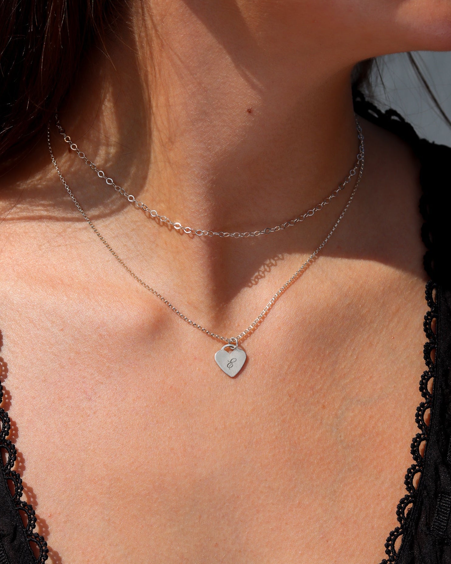 Sterling silver engraved heart pendant necklace layered with a delicate silver chain, styled in warm natural sunlight.