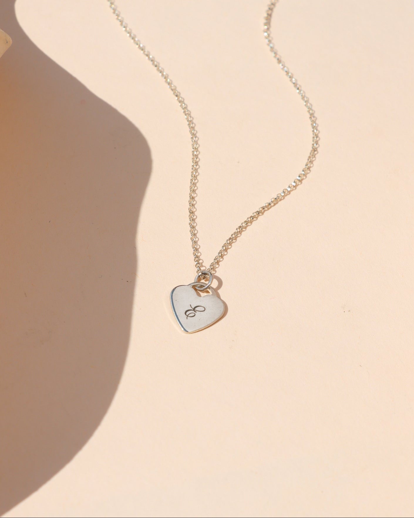 Sterling silver heart pendant necklace engraved with the letter E, styled in warm natural sunlight.