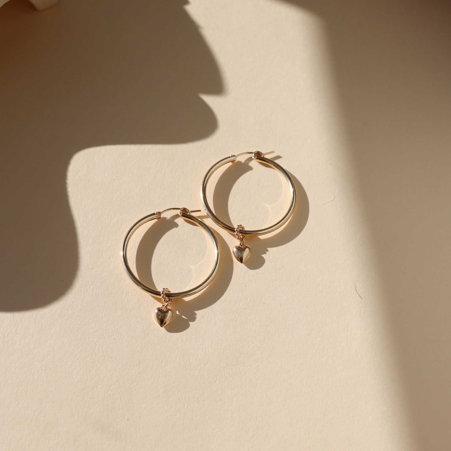 14k gold fill heart charm on large hoop earrings in the sunlight with shadows