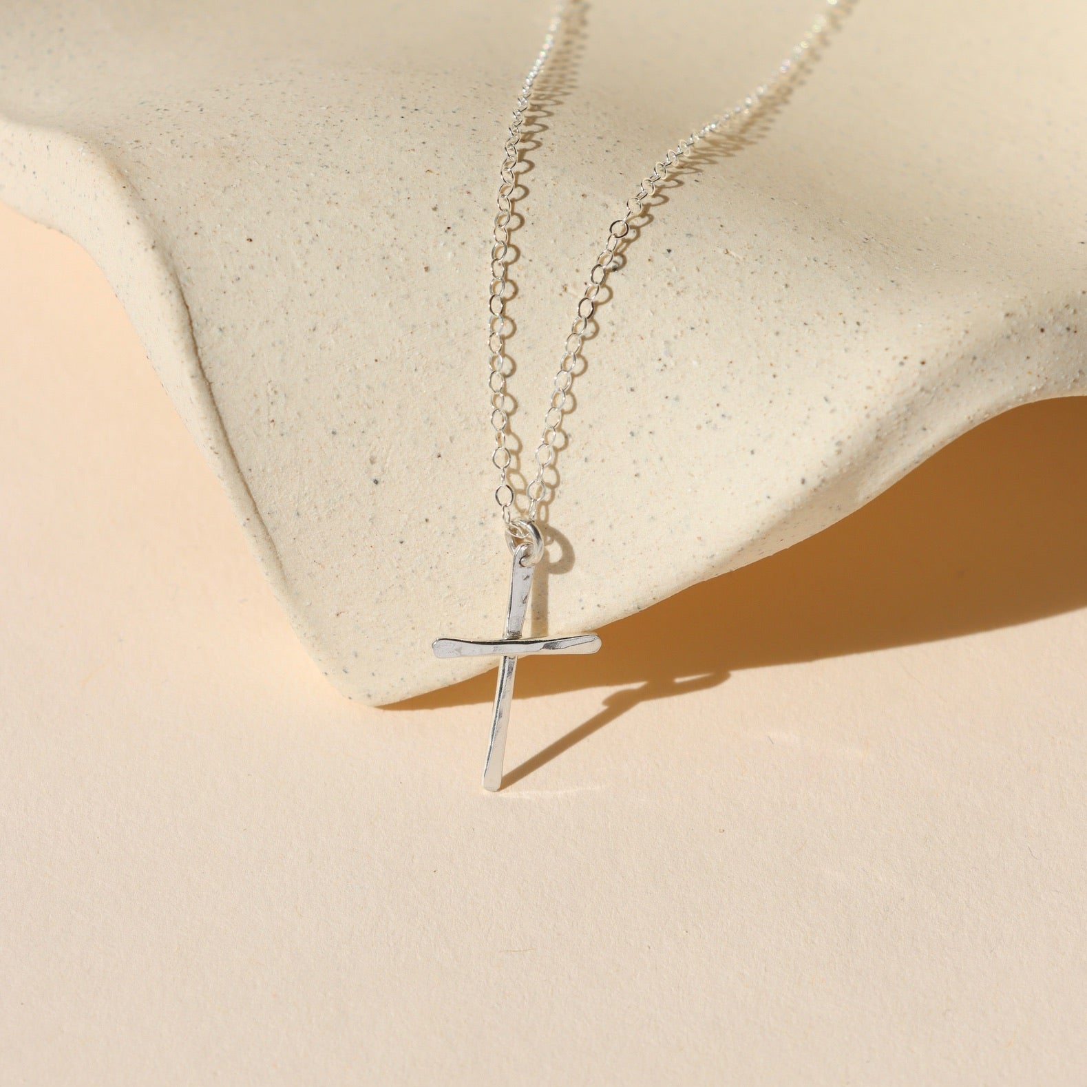 sterling silver hammered cross pendant on a delicate chain necklace on a light dish