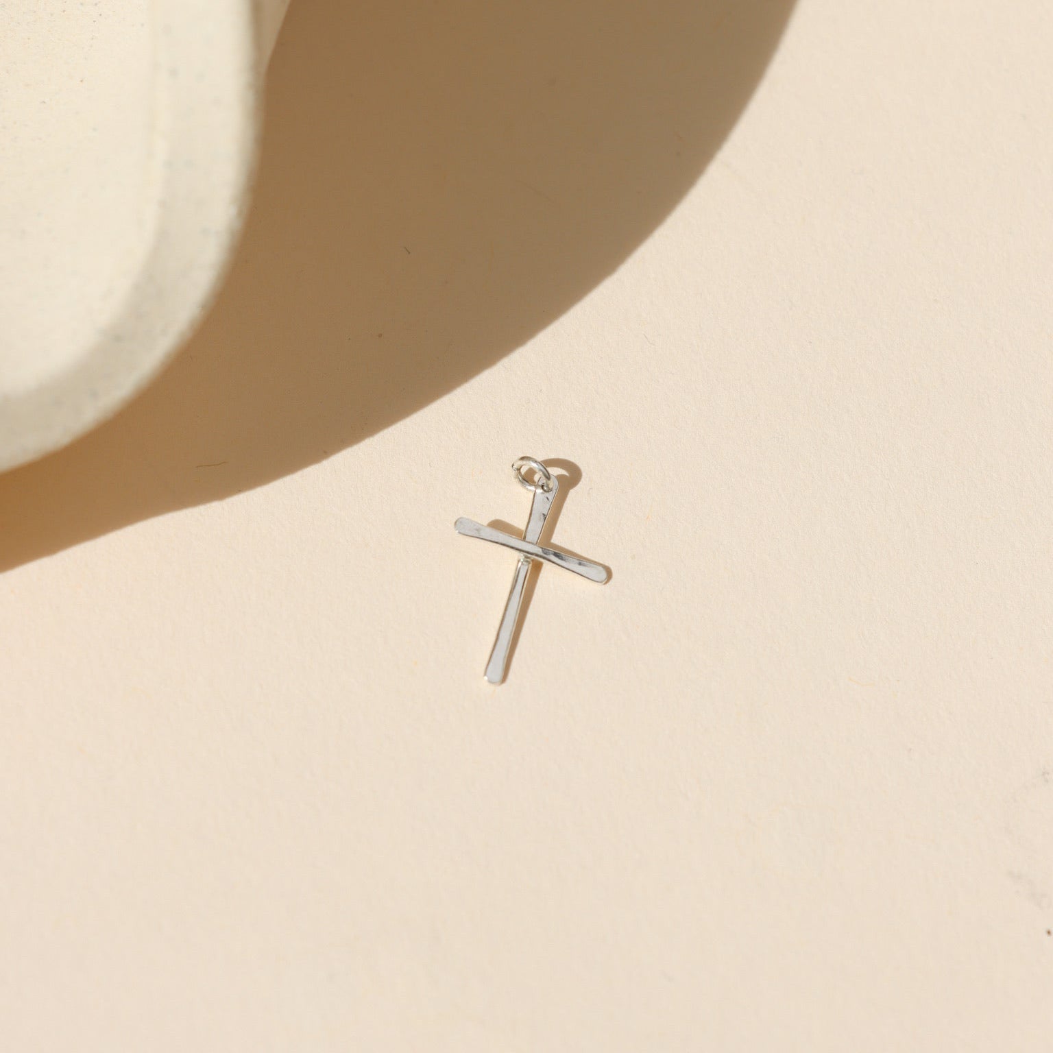 sterling silver handmade hammered cross charm on a light background