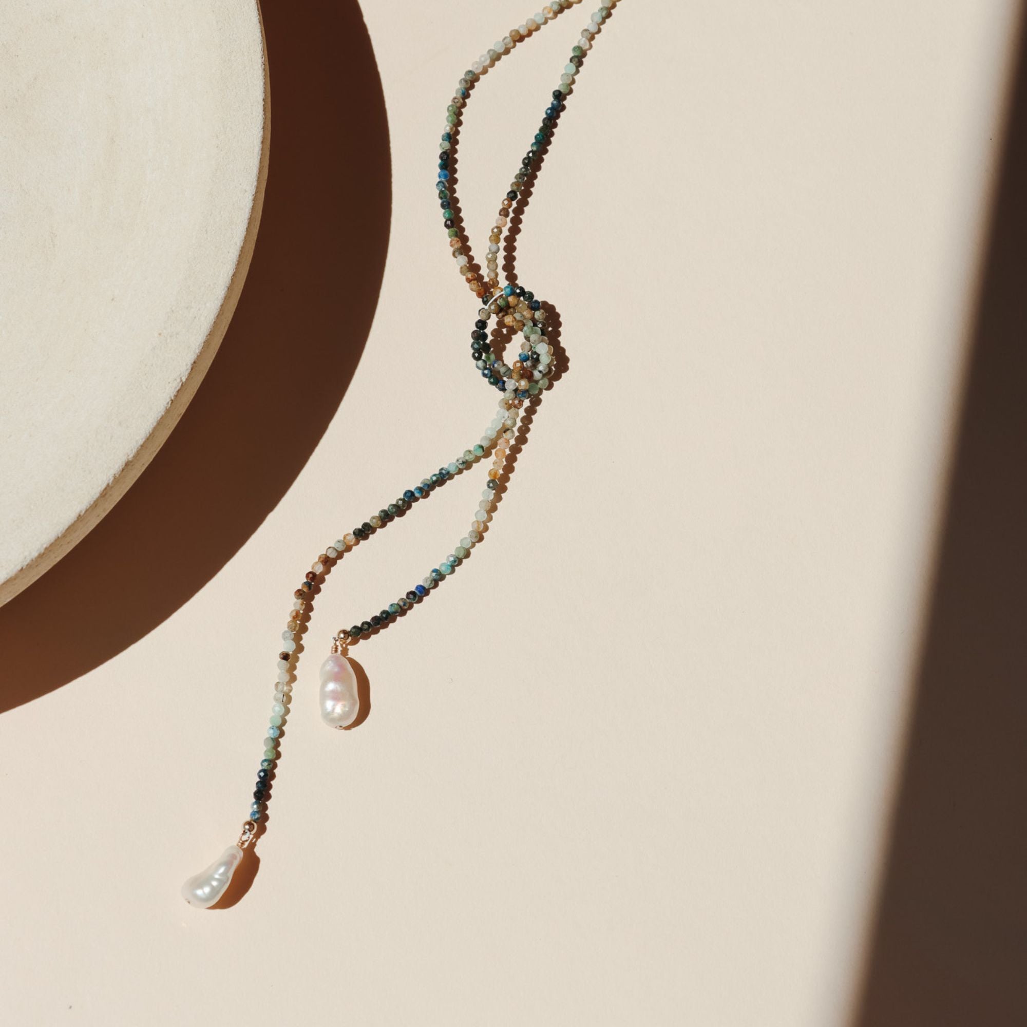beaded wrap necklace with large pearls on a light dish