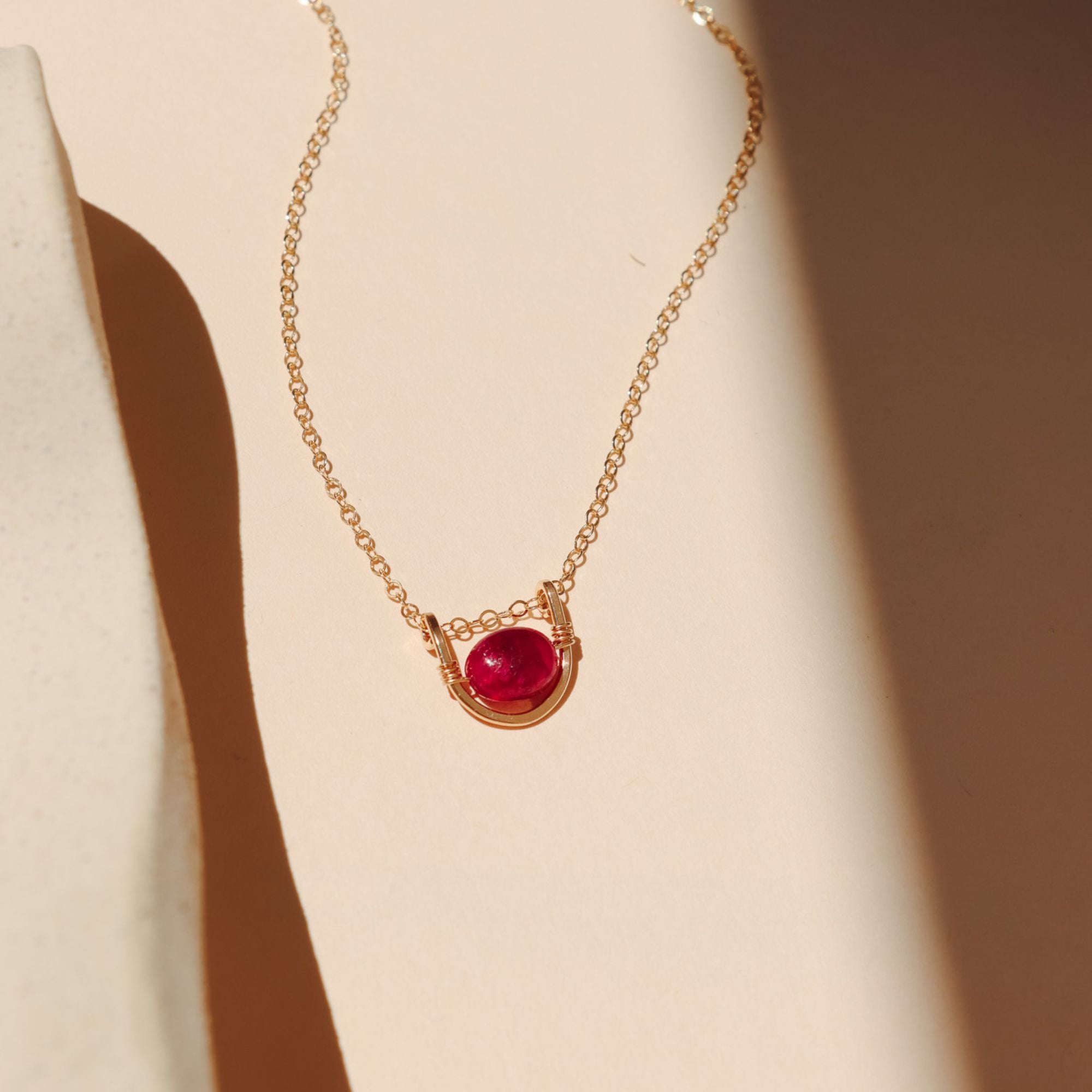 14k gold fill chain necklace with ruby and wire pendant on a light surface