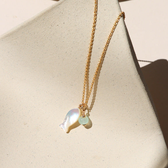 14k gold fill rolo chain necklace with mother of pearl fish and opal charms on a light dish