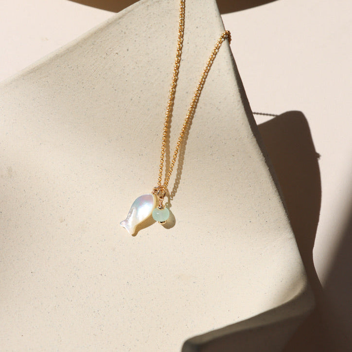 14k gold fill rolo chain necklace with mother of pearl fish and opal charms on a light dish
