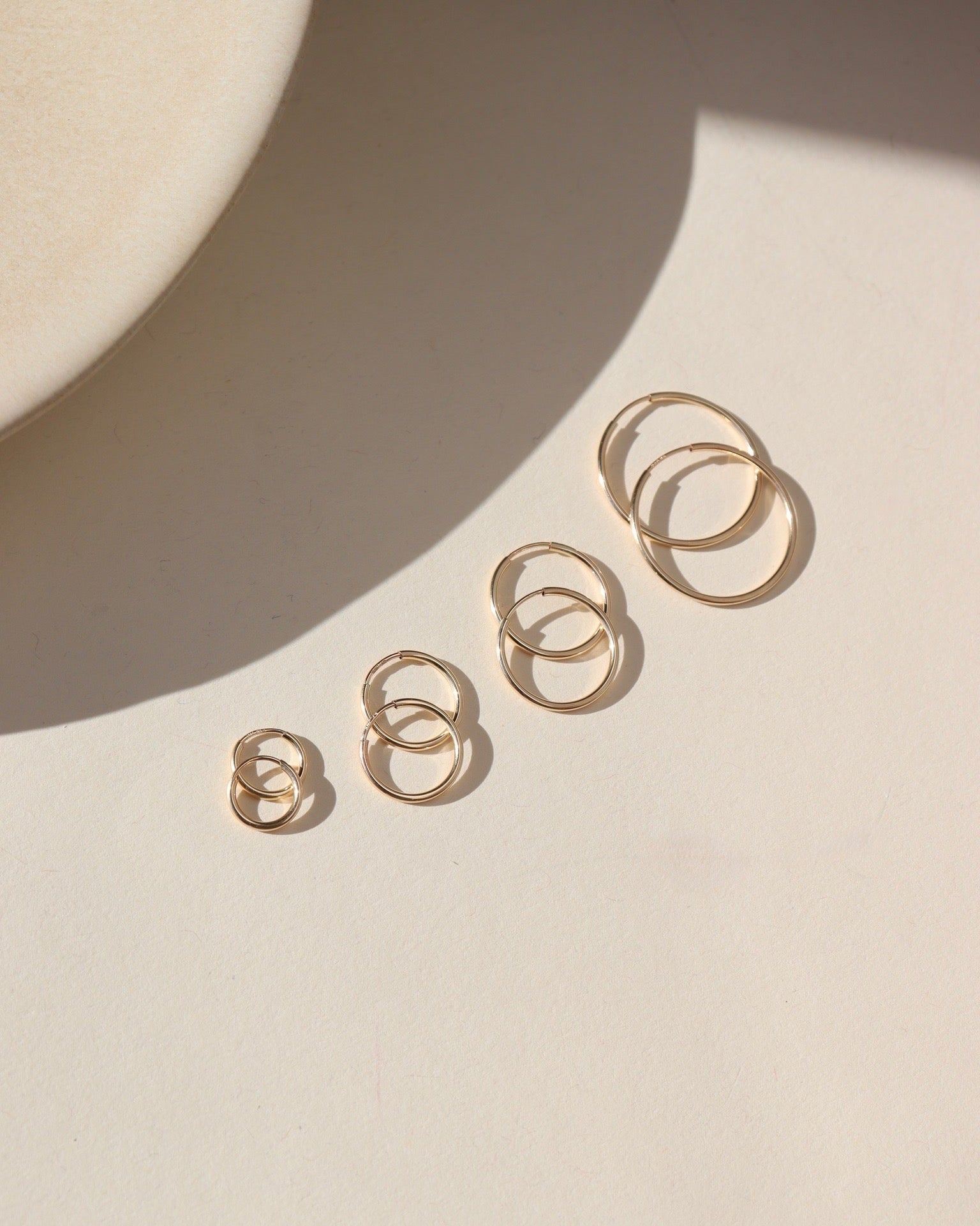 Product photo of Goldie Hoops, 14k gold fill endless hoop earrings in four graduated sizes, displayed on a light surface in warm natural sunlight.