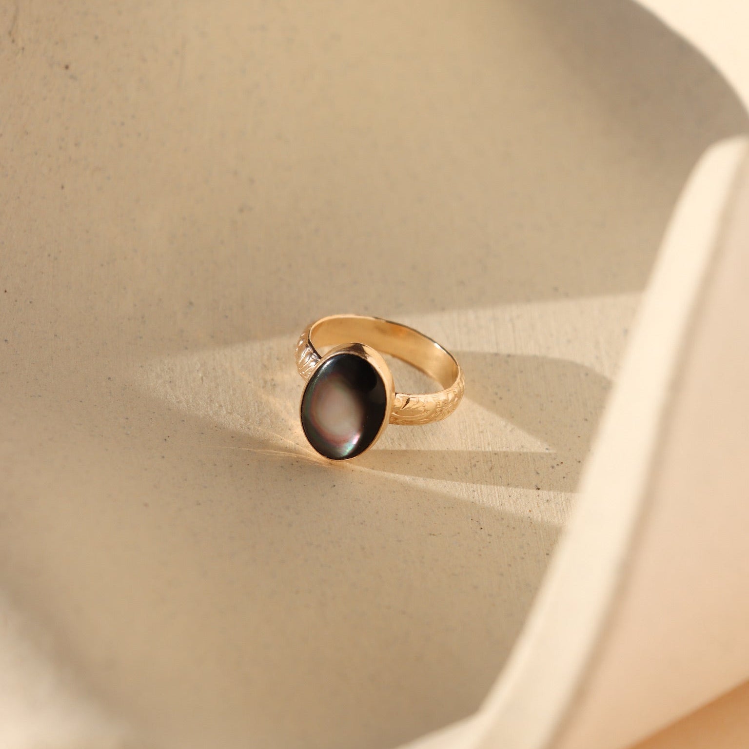 Moonflower rings in gold and silver with oval luminous stones, styled on a neutral surface in soft natural light.