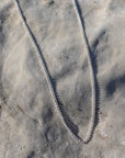 925 sterling silver la mer necklace laid on the beach in the sand.