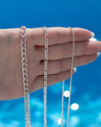 925 sterling silver La mer necklace, Gigi necklace, and Alex chain laid on a hand in the sunlight.