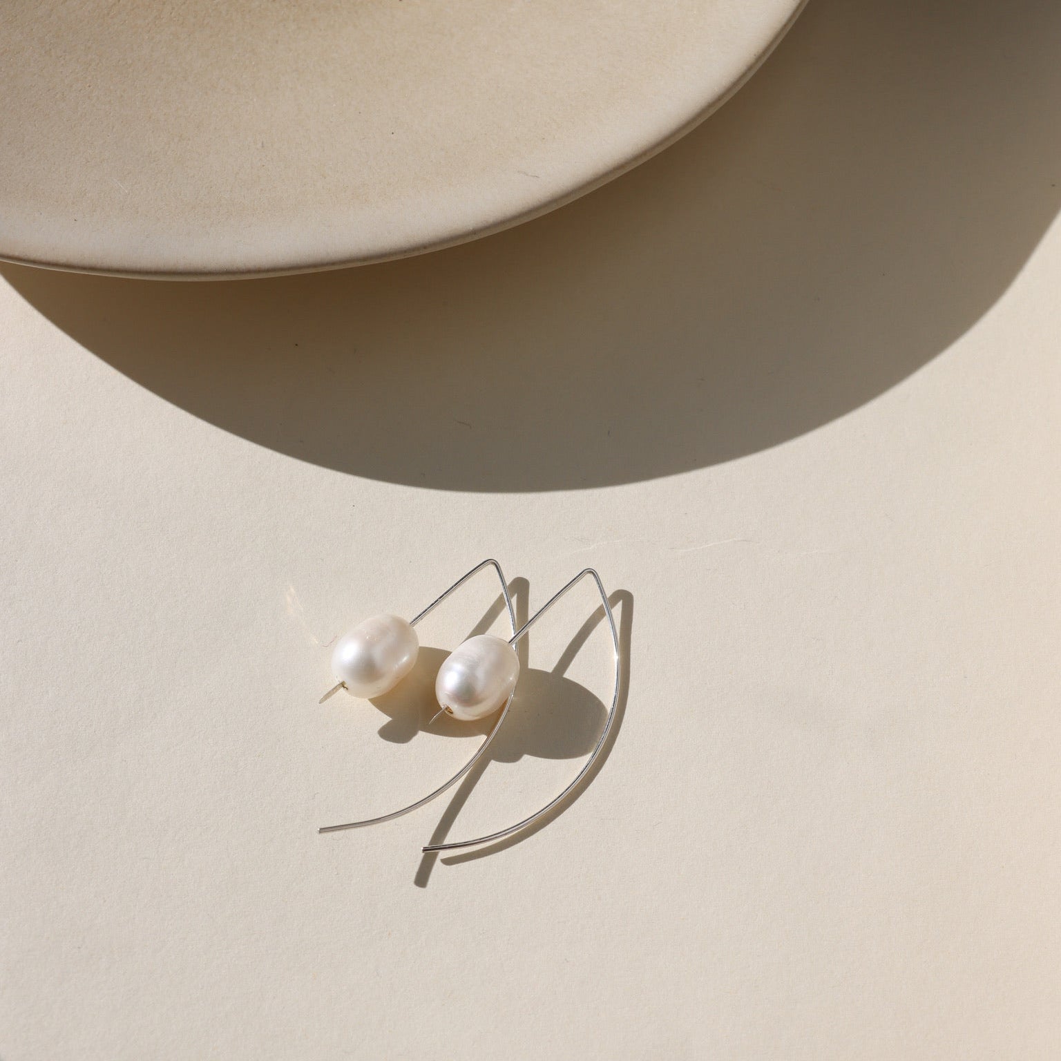 Delicate sterling silver half-moon earrings with smooth freshwater pearls set beneath a curved crescent design.