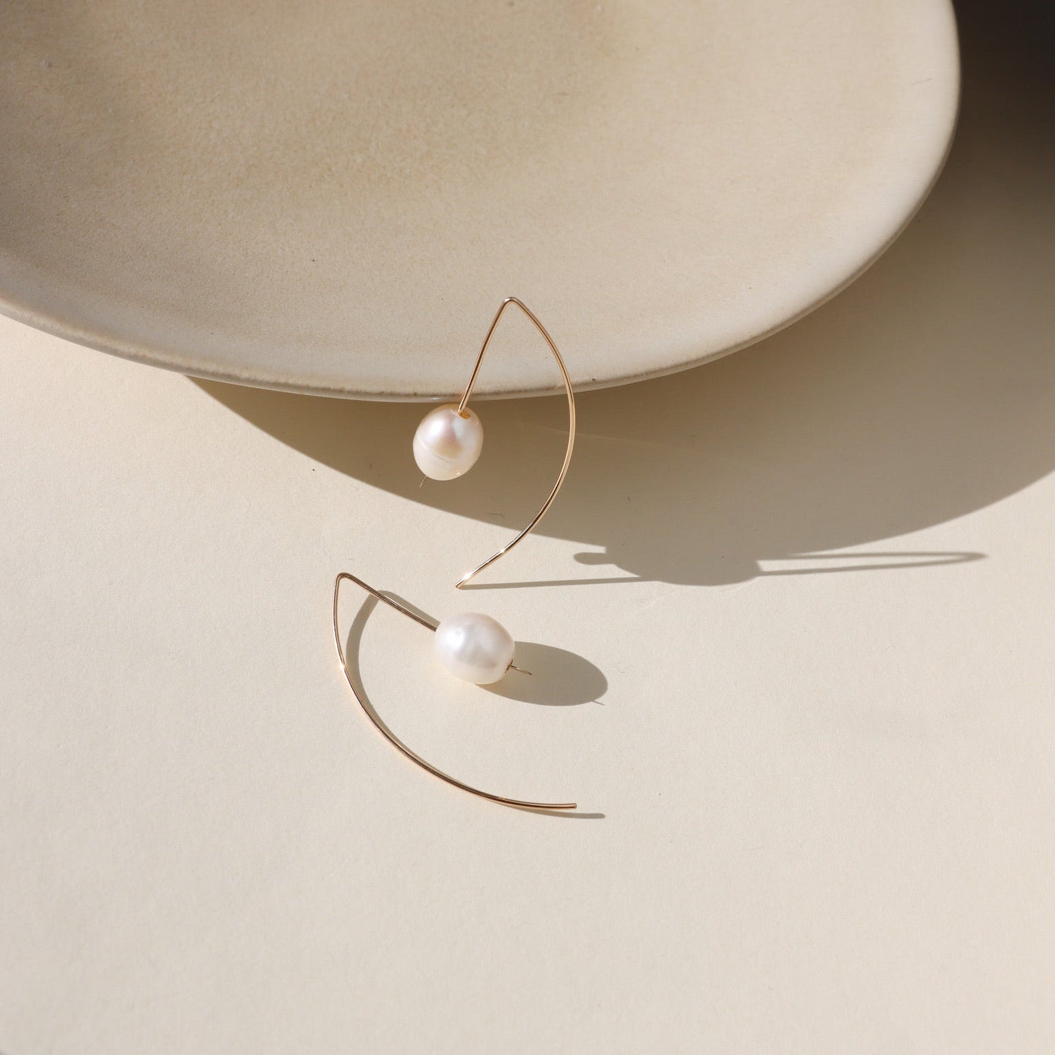 Delicate sterling silver half-moon earrings with smooth freshwater pearls set beneath a curved crescent design.