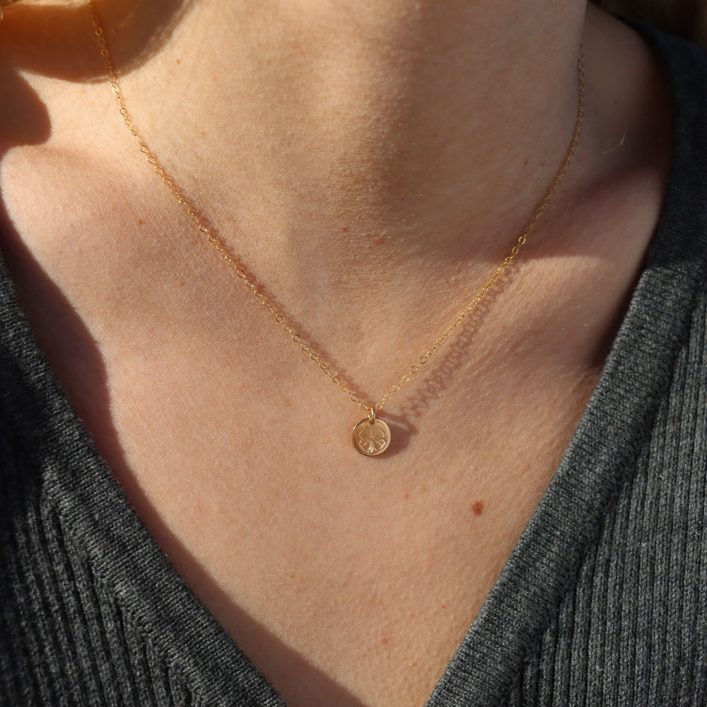 Close-up of a person wearing a gold necklace with a small four leaf clover pendant.
