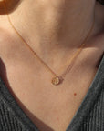 Close-up of a person wearing a gold necklace with a small four leaf clover pendant.