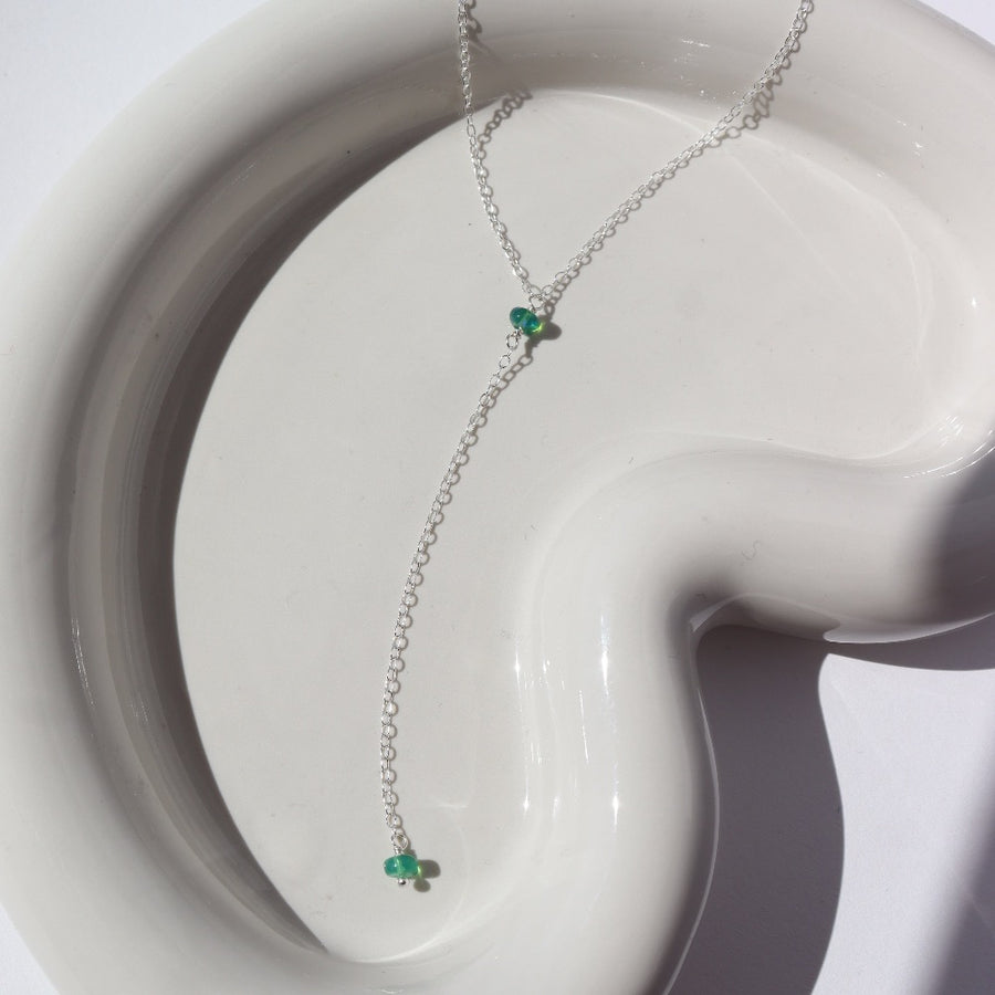 925 Sterling Silver Green opal lariat laid on a white plate in the sunlight. This necklace features our simple chain connected by the Green opal gemstone dangling on the lariat is another green opal lariat.