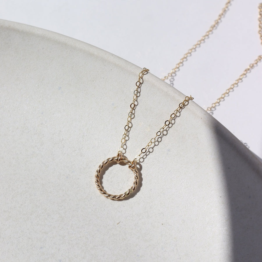 14k gold fill Spiral Necklace laid on a white plate in the sunlight. This necklace features the simple chain with the spiral eternity disc.