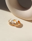 14k gold fill hoop earrings featuring a wave texture, photographed on a sunny table next to a ceramic dish on a white backdrop