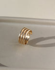 14k gold fill Trinity ring spirals into three bands, photographed on a ceramic dish. This ring features the look of the three layered band look but its only one ring.