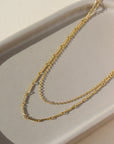 a 14k gold fill necklace made up of two chains, laid out on a sunny table