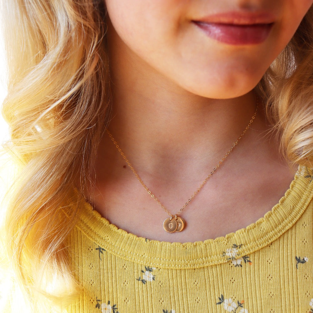 Model wearing 14k gold fill Tiny Monogram Disc Necklace. This necklace features our simple chain with a disc pendent with a heart stamped on it.