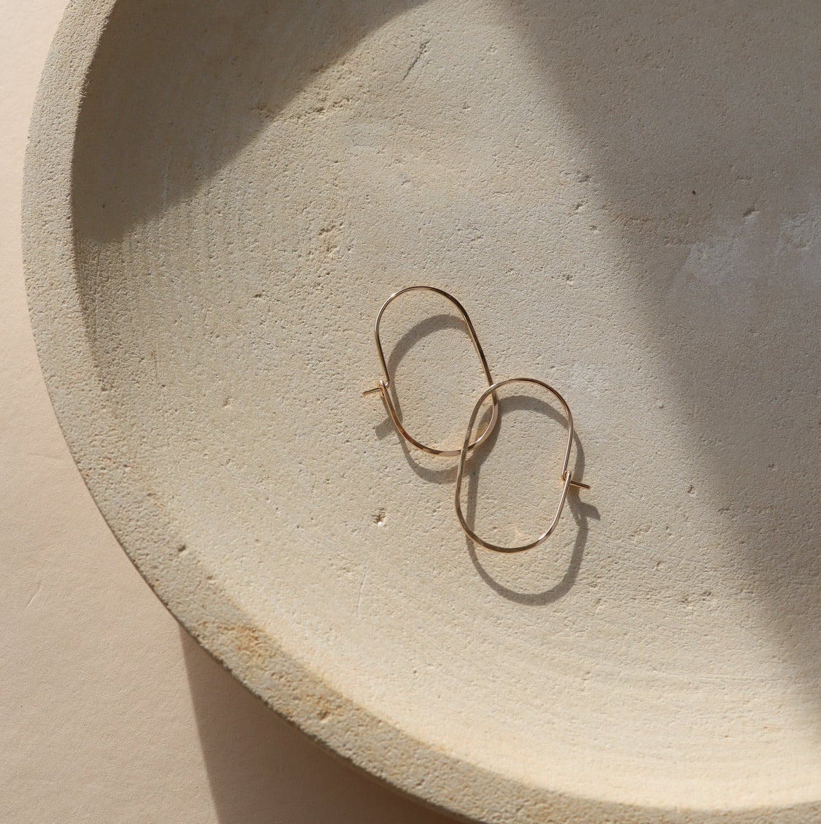 14k gold filled capsule hoops laid on a small plate