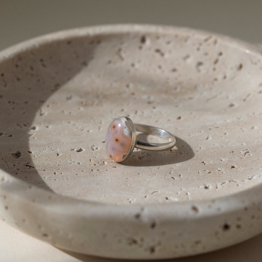 a sterling silver hand-set ocean jasper ring laid out on a cream colored backdrop in the sun