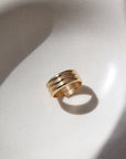 14k gold fill Trinity ring spirals into three bands, photographed on a white sunlit ceramic dish.This ring features the look of the three layered band look but its only one ring.