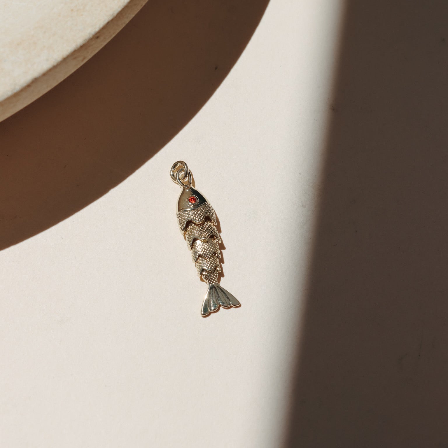 Large gold koi fish charms with red crystal eyes displayed on a neutral surface in warm natural light with shadowing.