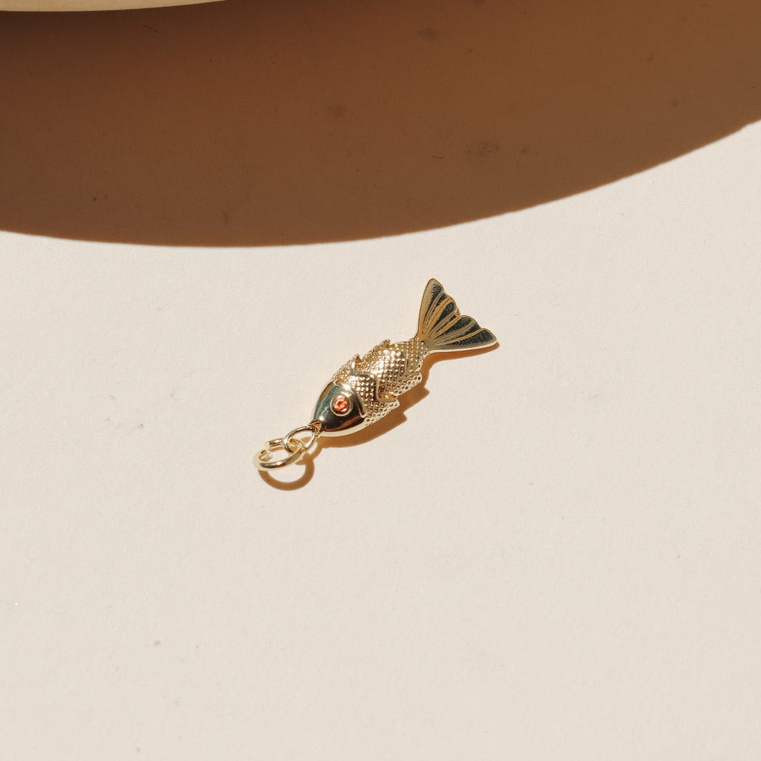 Small gold koi fish charms with red crystal eyes displayed on a neutral surface in warm natural light.