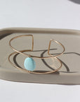 14k gold fill double wire cuff bracelet featuring a large turquoise stone wired to the middle. Photographed on a taupe dish in the sunlight