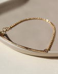 14k gold fill Bar Anklet laid on a tan dish in the sunlight- Token Jewelry