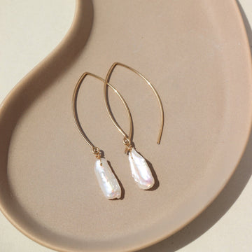 14k Gold fill Juno Earrings laid on a tan plate in the sunlight. Perfect for your wedding fits.