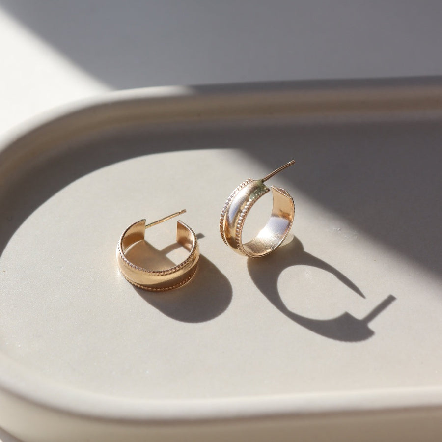 14k gold fill small hoop stud earrings featuring a textured outside band, photographed on a ceramic dish | handmade by Token Jewelry in Eau Claire, Wisconsin